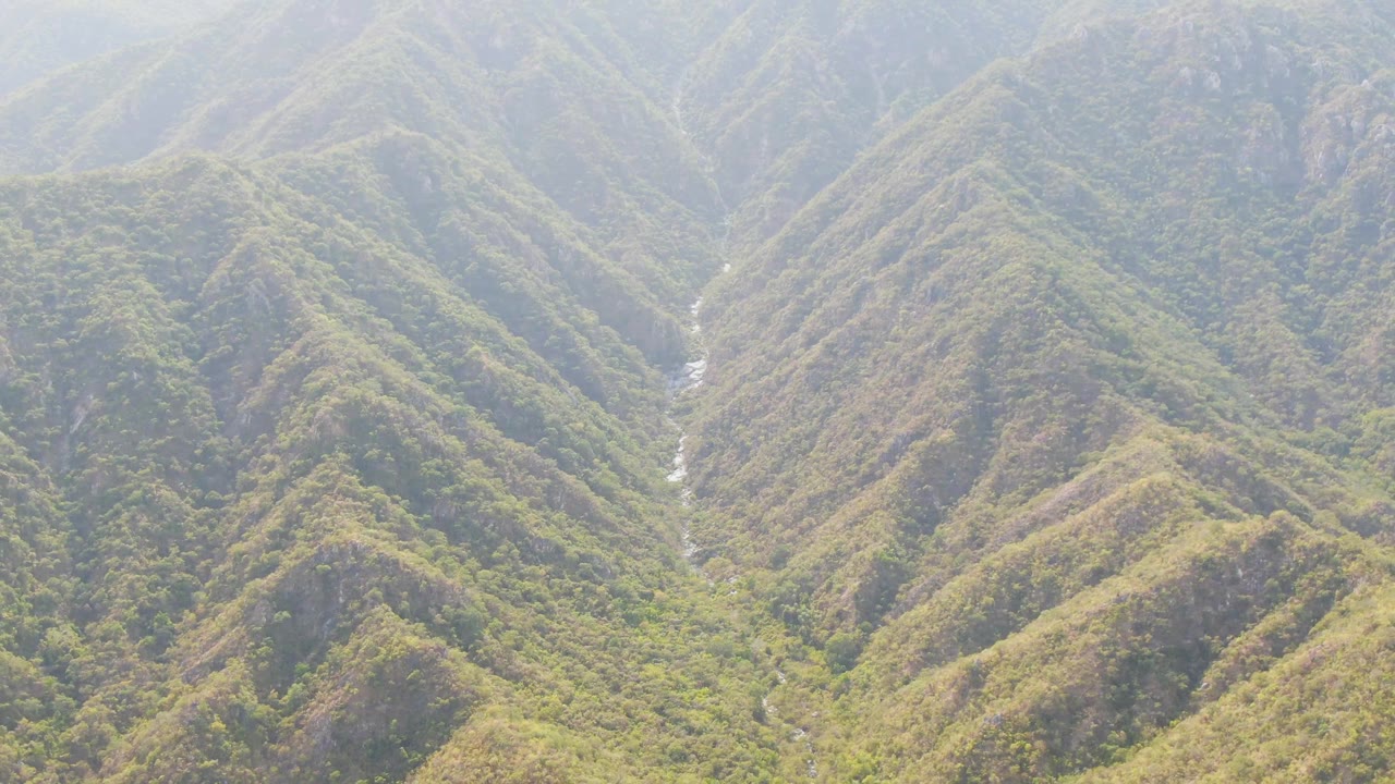 Aerial view in San Dionisio, Baja California Sur, with layered ridgelines, mixed green vegetation, exposed brown terrain, and no visible people.