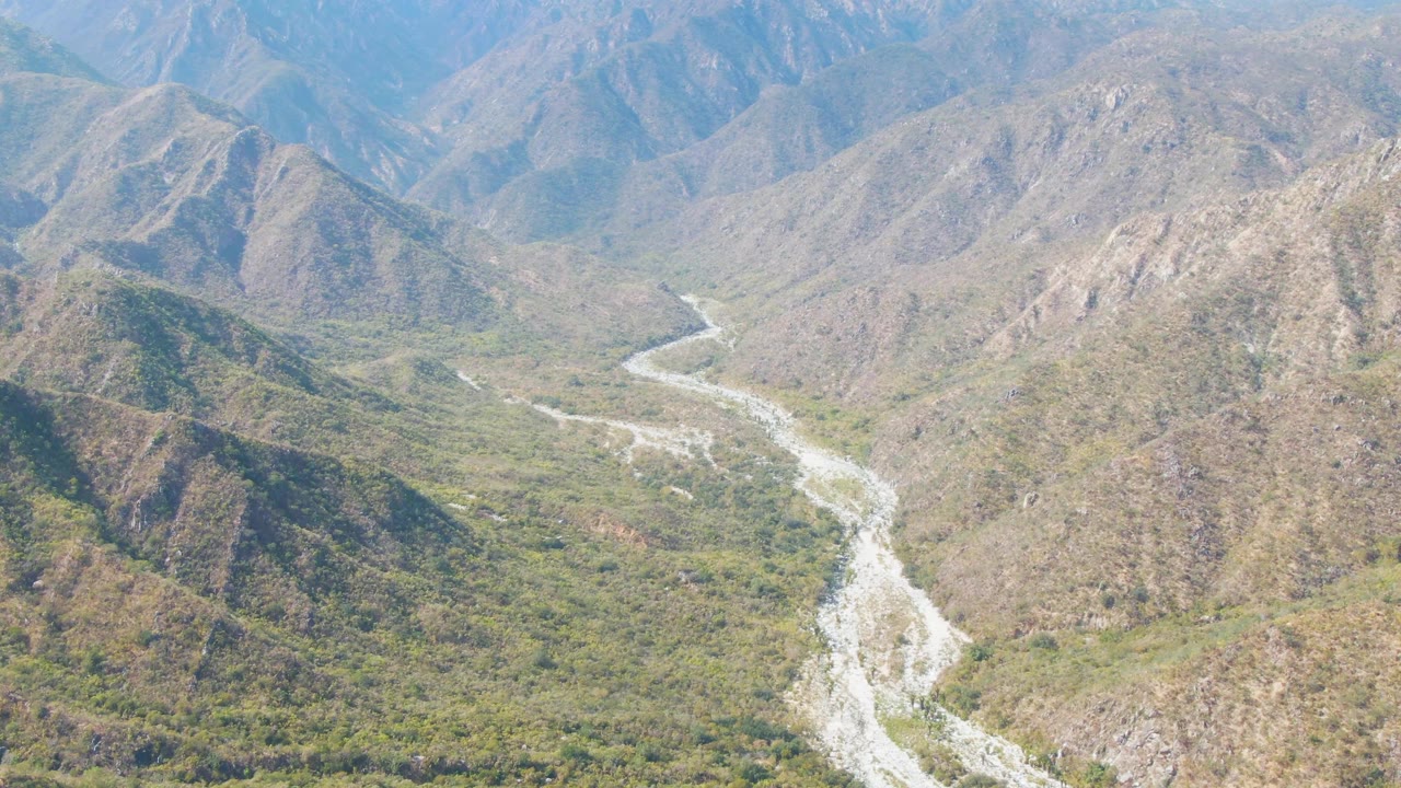 Aerial view of a winding pale riverbed through green and brown mountains