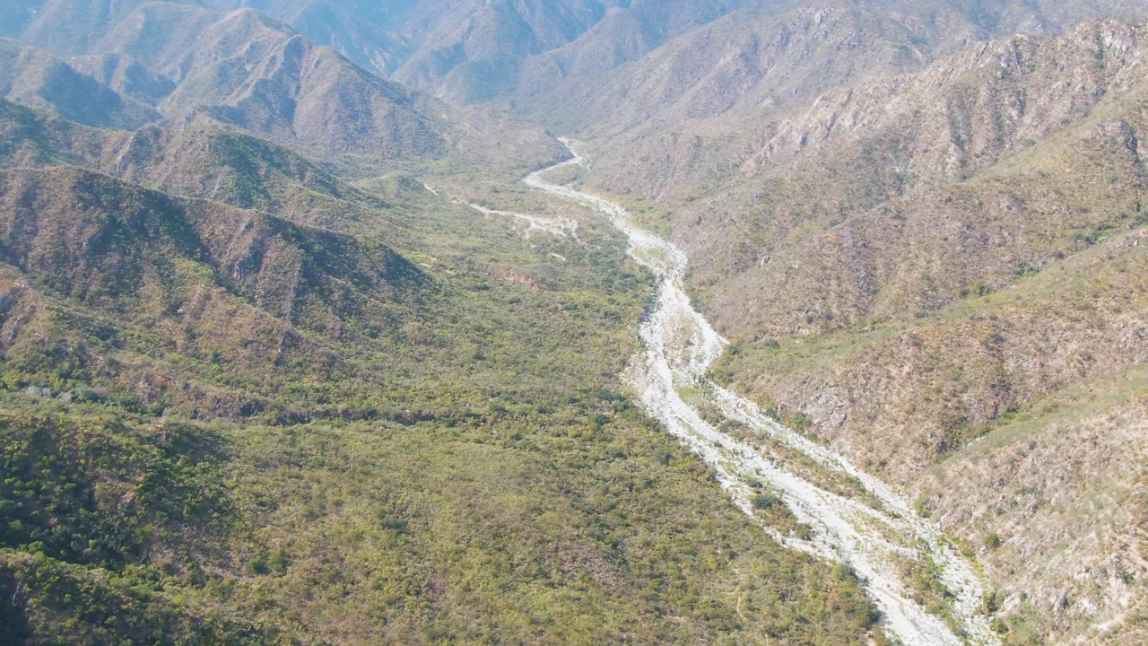 A high aerial view in San Dionisio, Baja California Sur shows the river channel curving from the distant valley toward the foreground between dry, rocky hills, with no visible people.