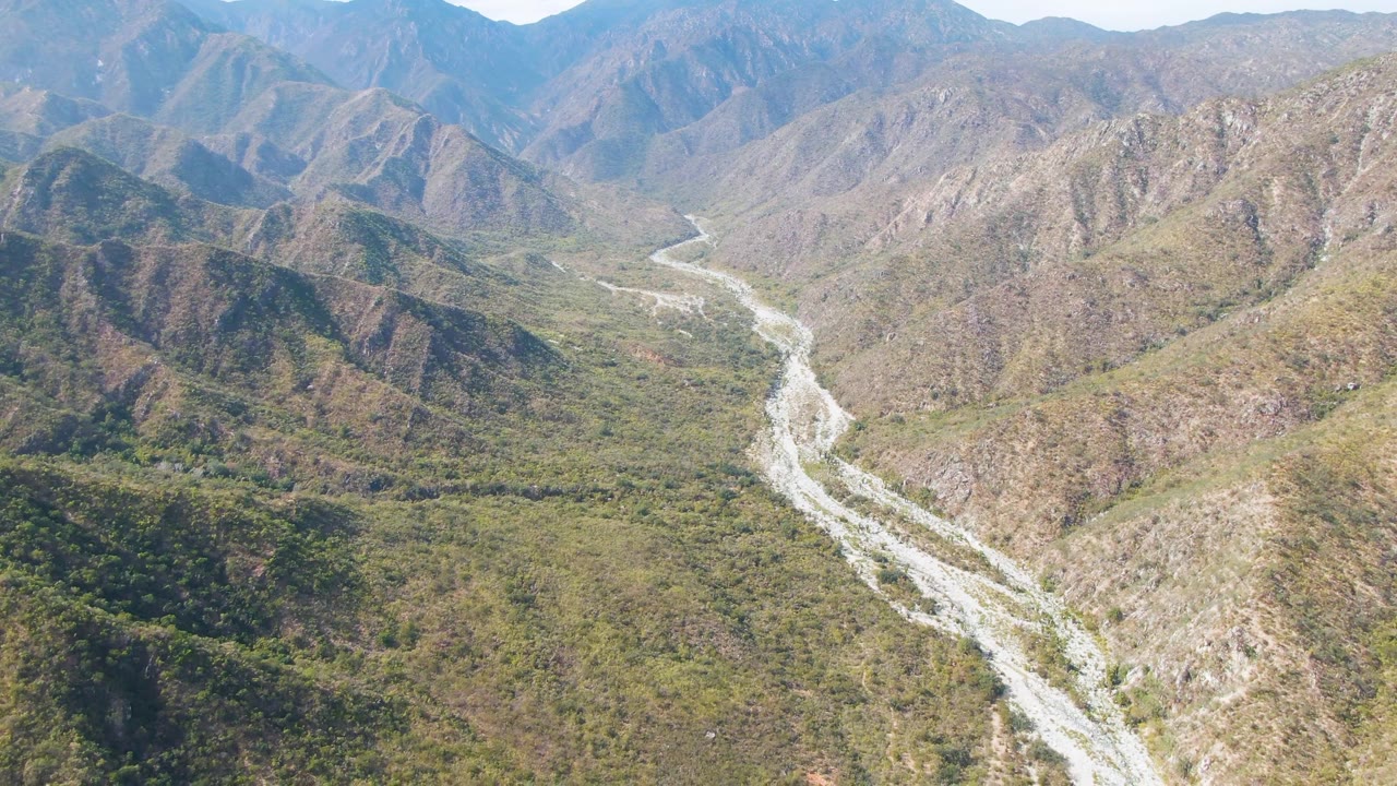 Riverbed bends through green and brown hills in a remote mountain valley.