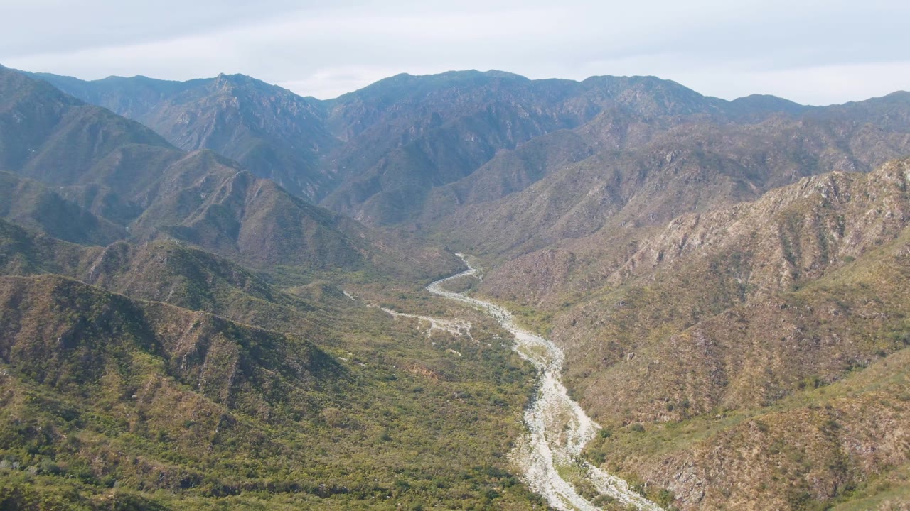 Aerial view in San Dionisio, Baja California Sur, with a pale river running through a green and brown mountain valley and no visible people.