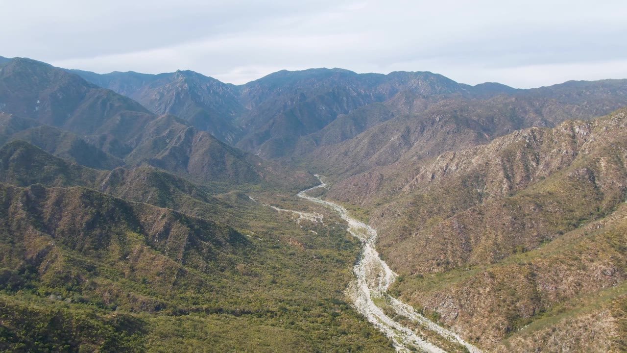 Aerial landscape in San Dionisio, Baja California Sur, showing a bright braided-looking river channel across the center of a rugged green and brown valley with no visible people.