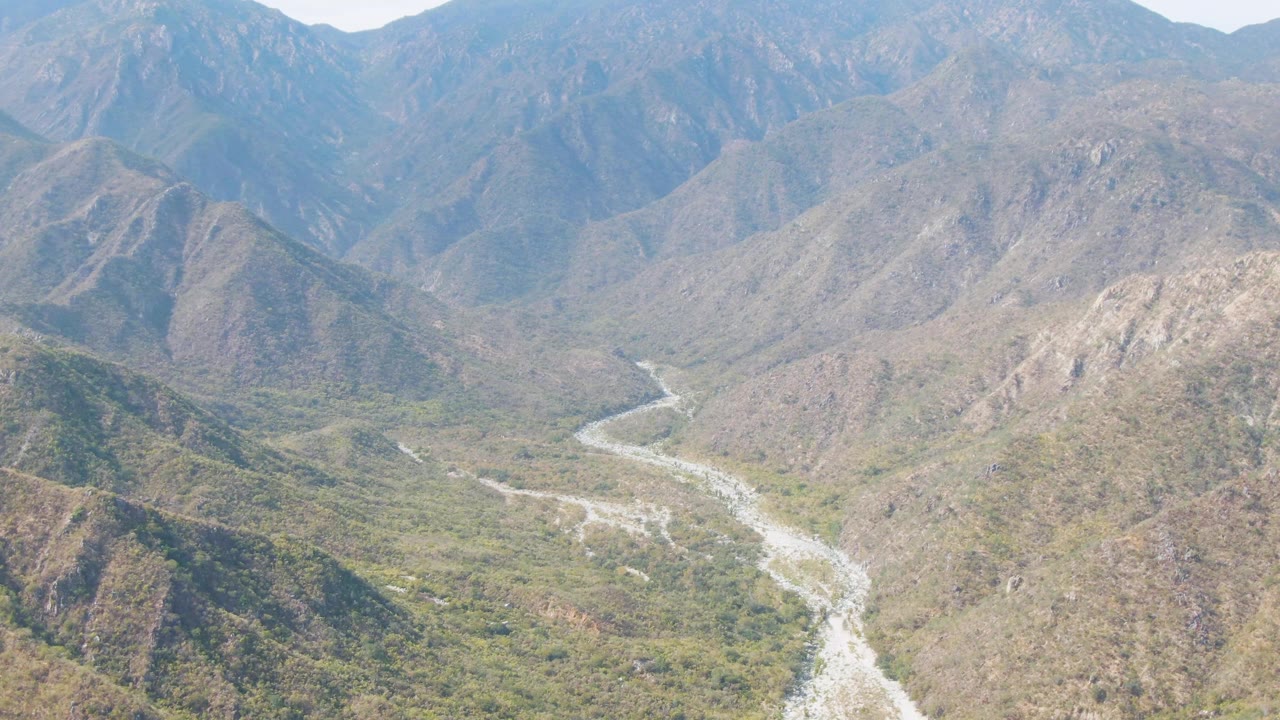 Aerial frame from San Dionisio, Baja California Sur showing a pale winding river running through a broad mountain valley, with no visible people.