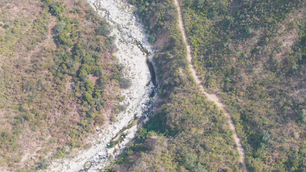 Aerial view of a rocky riverbed and dirt path through scrubby hills.