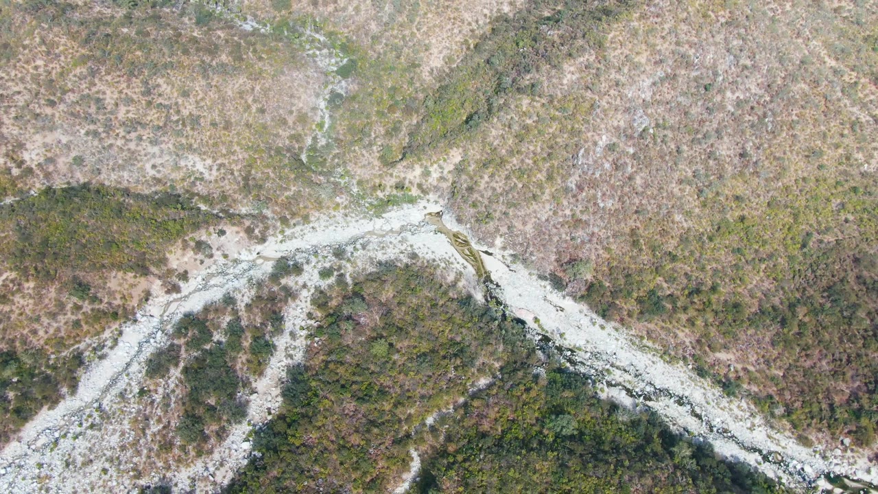 Top-down frame in San Dionisio, Baja California Sur, showing a light-toned road or wash branching through rough hills with scattered vegetation and no visible people.