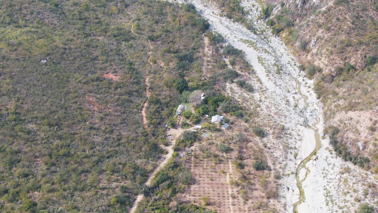 Wide aerial view of a pale riverbed beside scrub-covered hills