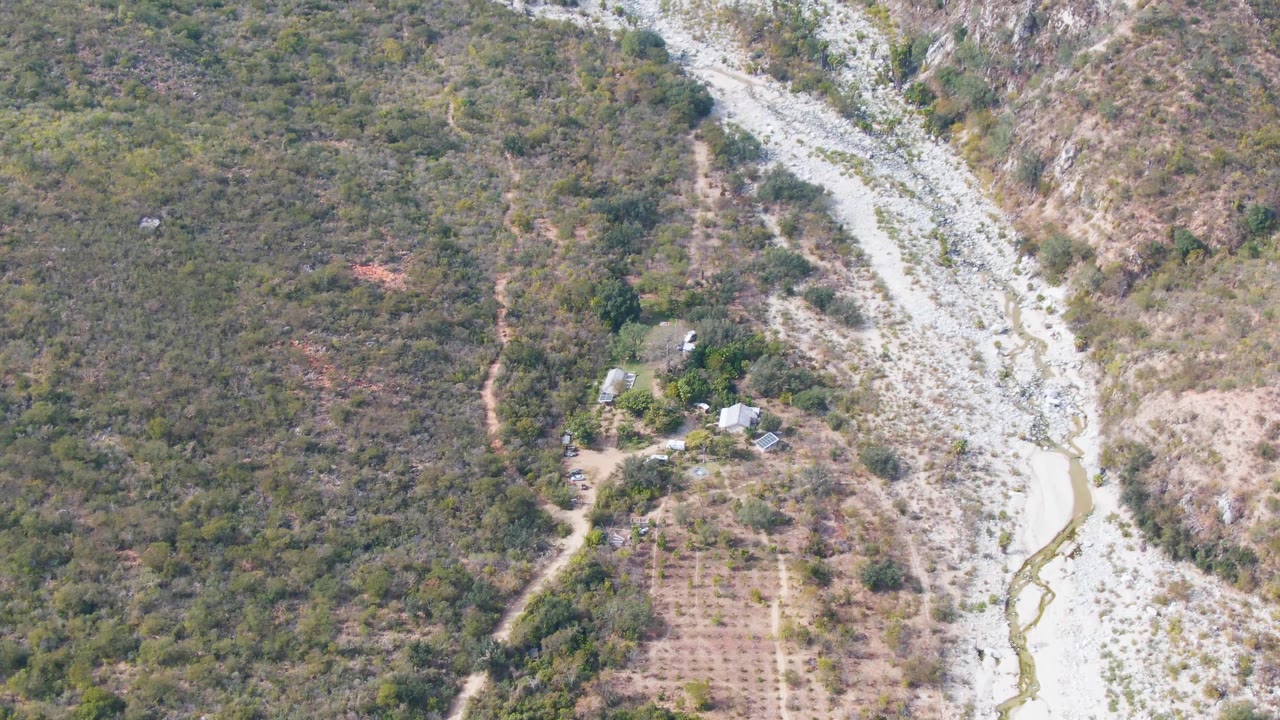 Aerial view in San Dionisio, Baja California Sur, where the light rocky stream channel bends through the valley with dense brush on the left slope and no visible people.