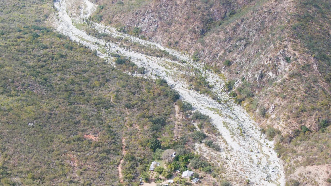 Aerial frame from San Dionisio, Baja California Sur showing the light gravel route bending through a dry rocky corridor, with scrub on both sides and no visible people.
