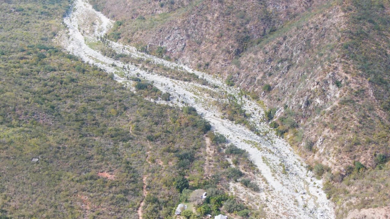Wider aerial view of the winding route with rocky hillside and sparse green vegetation.