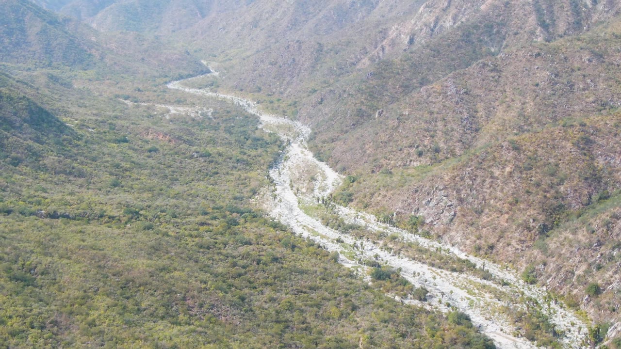 Aerial view looking down a valley where a light riverbed curves around a rocky hill.