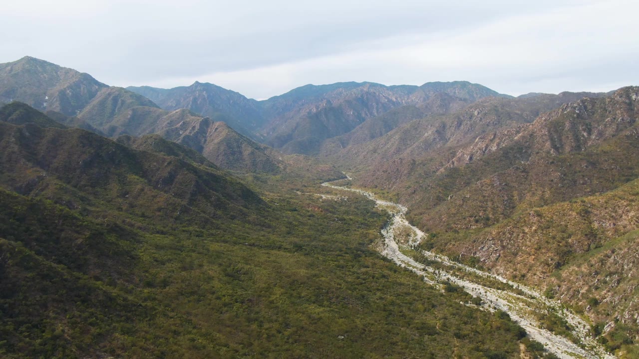 Aerial valley view with a bright riverbed between steep green-brown hills.