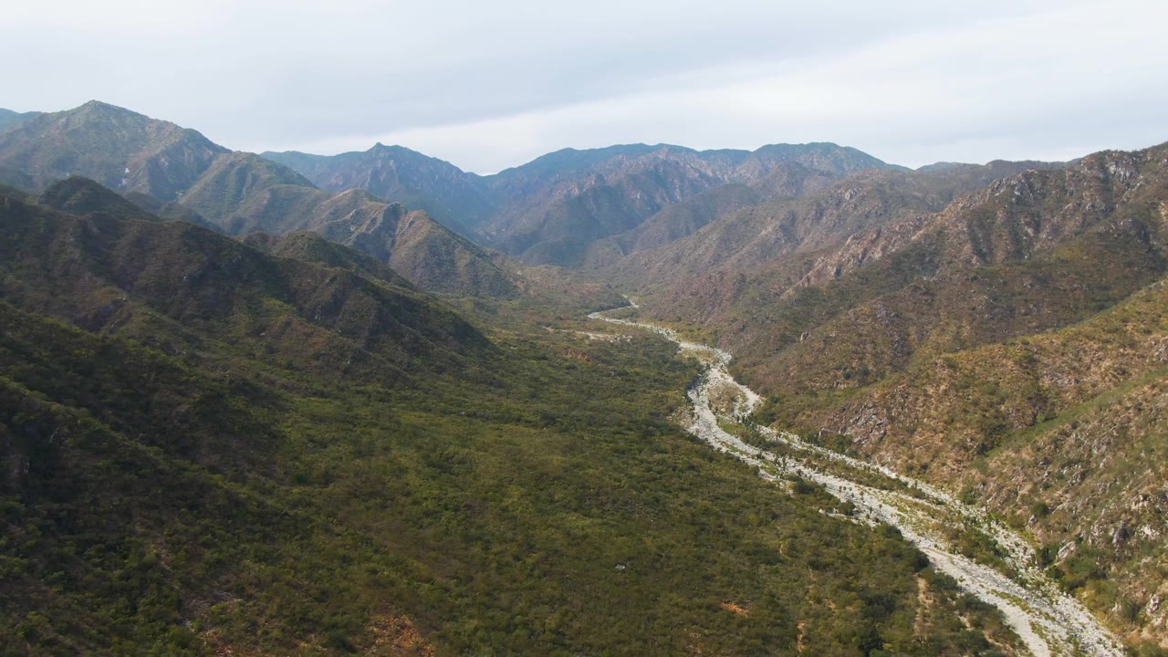 The frame looks over San Dionisio's rocky river channel and broad green valley floor, with brown ridgelines rising on both sides and no visible people.