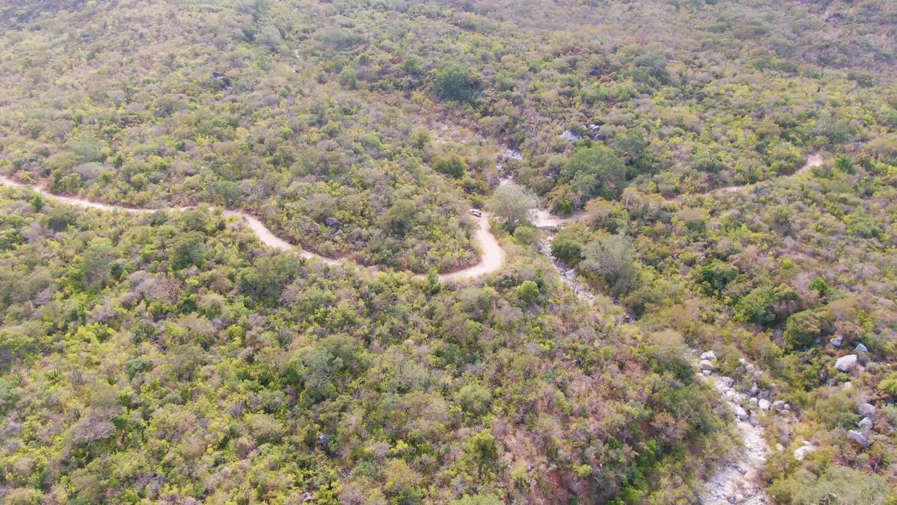 Aerial hillside view with a dirt road bend and rocky stream bed below.