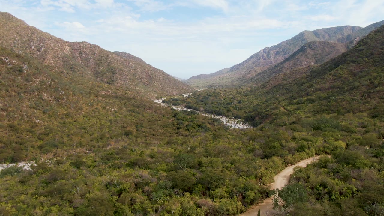 Wide mountain valley with dirt road, vegetation, and distant riverbed
