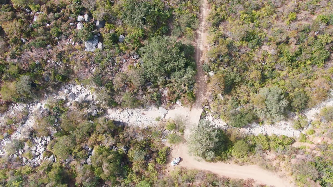 Overhead view of a white car on a dirt road through brush and rocks.