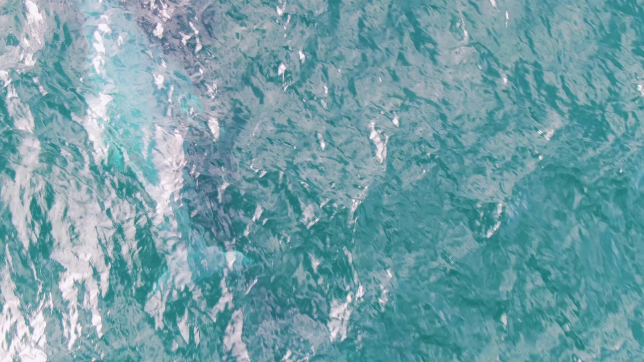 Overhead turquoise ocean surface with pale foam streaks