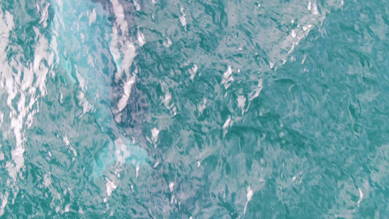Blue-green ocean surface at Shipwrecks, Baja California Sur, with scattered white streaks, mottled underwater tones, and no visible people.