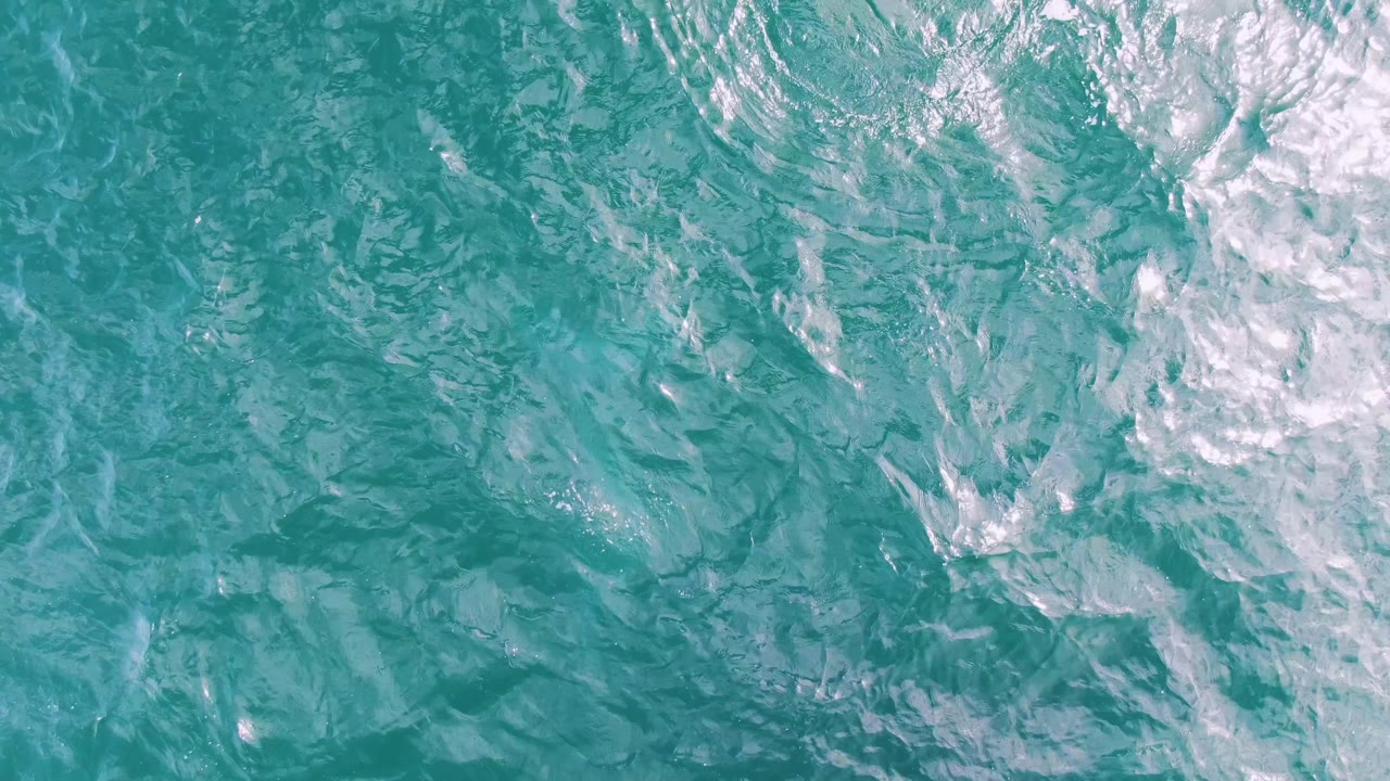 Top-down view of turquoise ocean water at Shipwrecks, Baja California Sur, with white foam gathered toward the upper right and no visible people.
