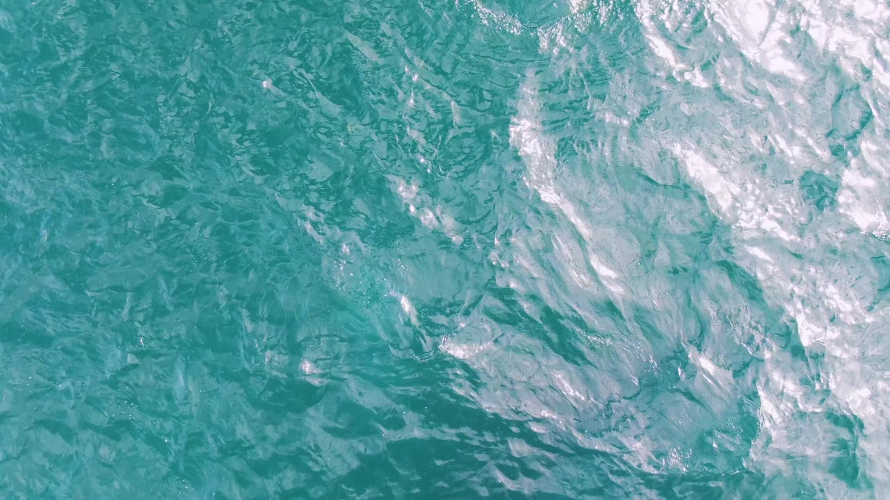 Overhead frame of blue-green water at Shipwrecks, Baja California Sur, where pale foam patches spread across the upper half and no visible people appear.