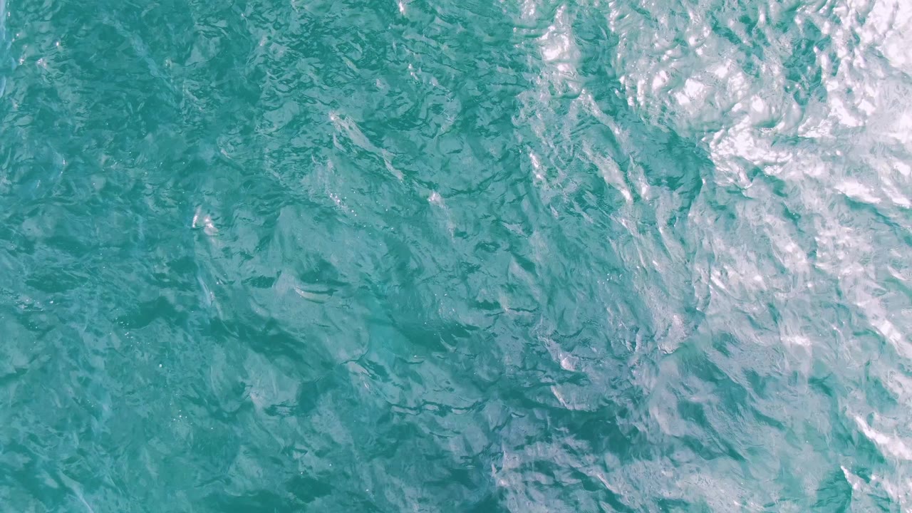 Top-down ocean surface at Shipwrecks, Baja California Sur, with dense white foam near the upper right edge, darker teal ripples below, and no visible people.