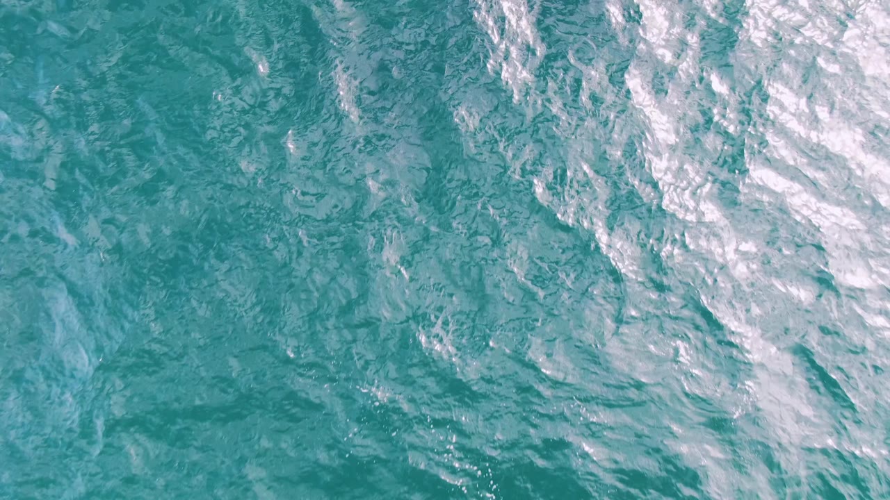 Blue-green ocean water at Shipwrecks, Baja California Sur, with softer ripples across the center, bright shimmer near the upper right, and no visible people.