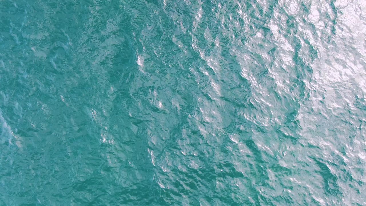 Open turquoise ocean at Shipwrecks, Baja California Sur, with faint diagonal ripples, pale foam or glare near the right edge, and no visible people.