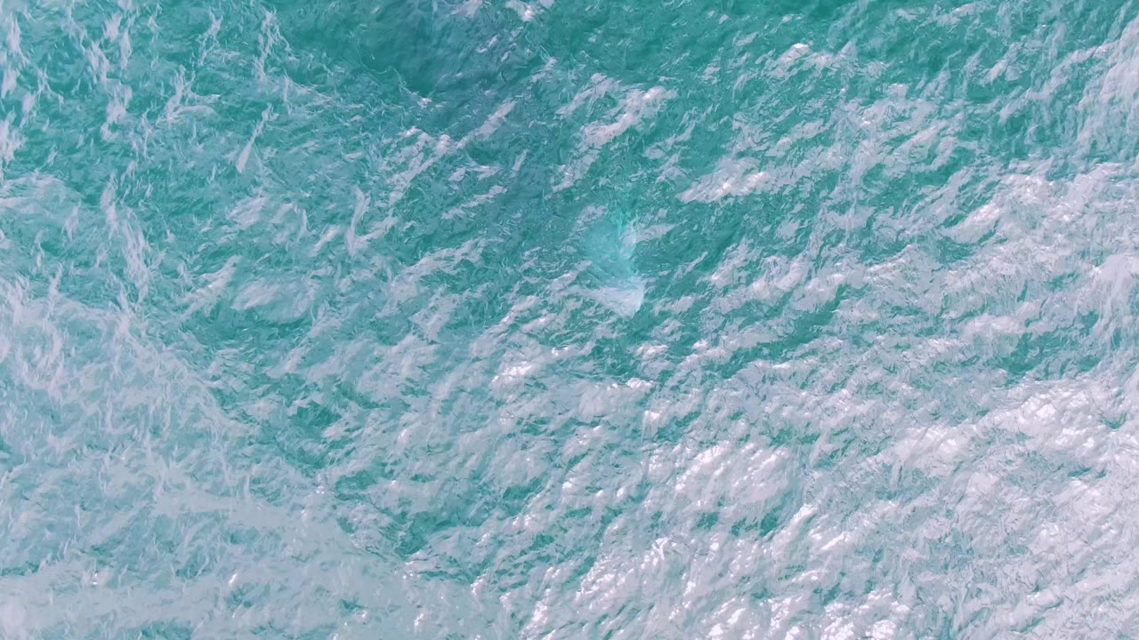 Aerial-looking frame of turquoise water at Shipwrecks, Baja California Sur, with denser white foam crossing the center and no visible people.