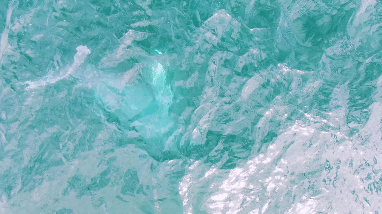 Turquoise ocean surface at Shipwrecks, Baja California Sur, with streaked white froth and scattered bright reflections, no visible people.