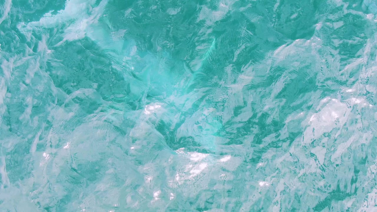 Overhead view of turquoise water in Shipwrecks, Baja California Sur, where white foam patches mix into rippled surface texture with no visible people.