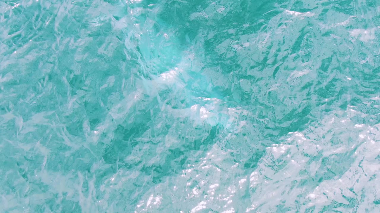 Turquoise ocean surface at Shipwrecks, Baja California Sur, with paler foam patches spread wider across ripples and no visible people.