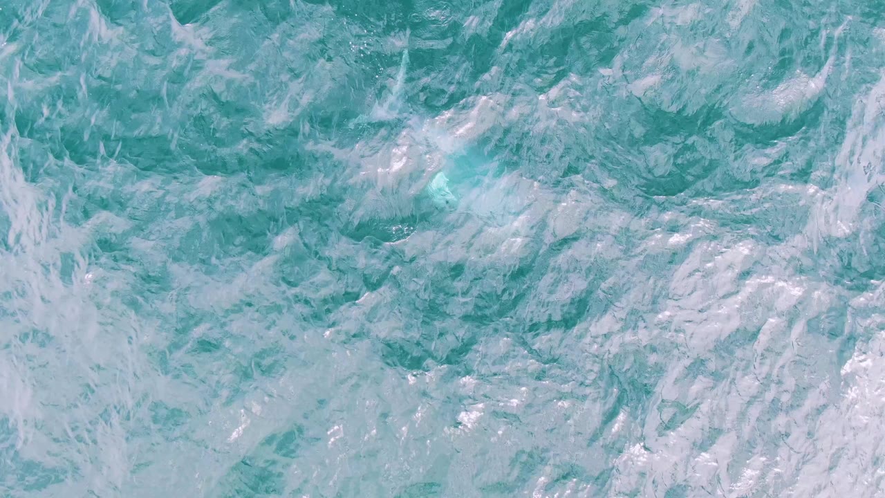 Close overhead frame of teal ocean at Shipwrecks, Baja California Sur, where pale foam gathers in broad streaks across the water with no visible people.