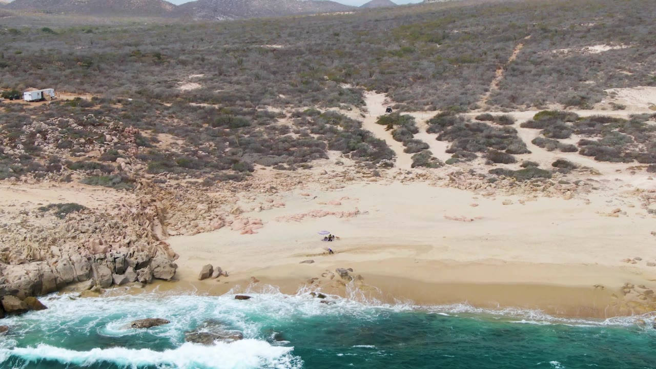 Drone view of waves breaking below a sandy beach and rocky cliff