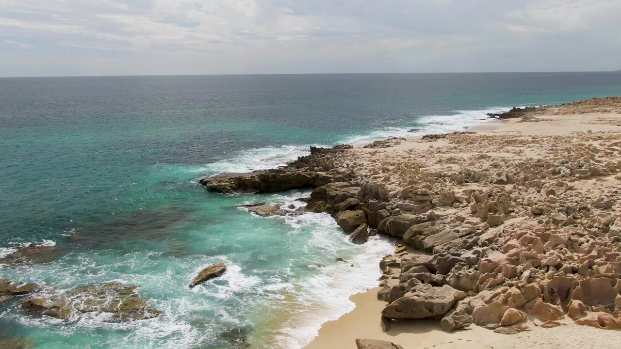 Ocean waves recede from a sandy cove bordered by rocky outcrops.
