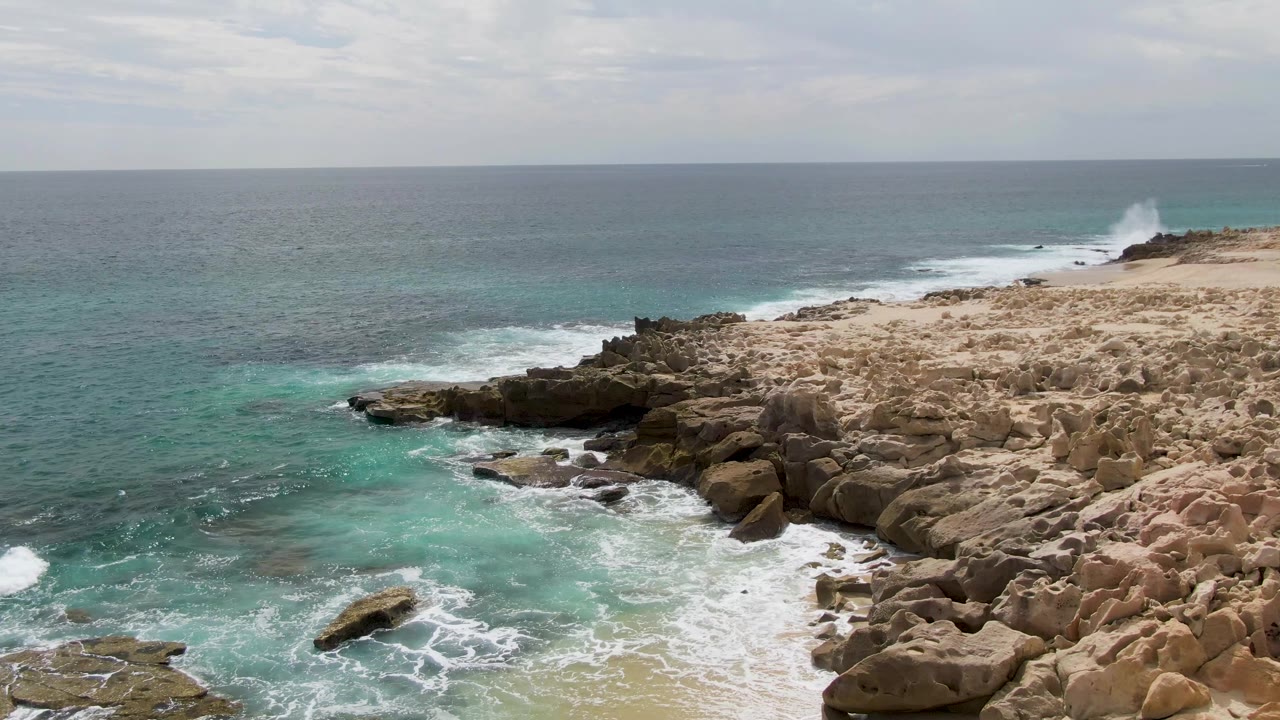 Rocky coastline with turquoise surf and overcast sky.