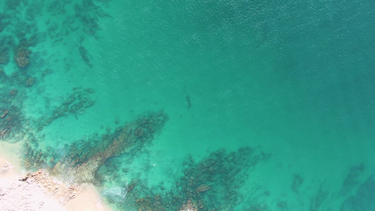 Pale beach edge and turquoise shallows with underwater rock patches