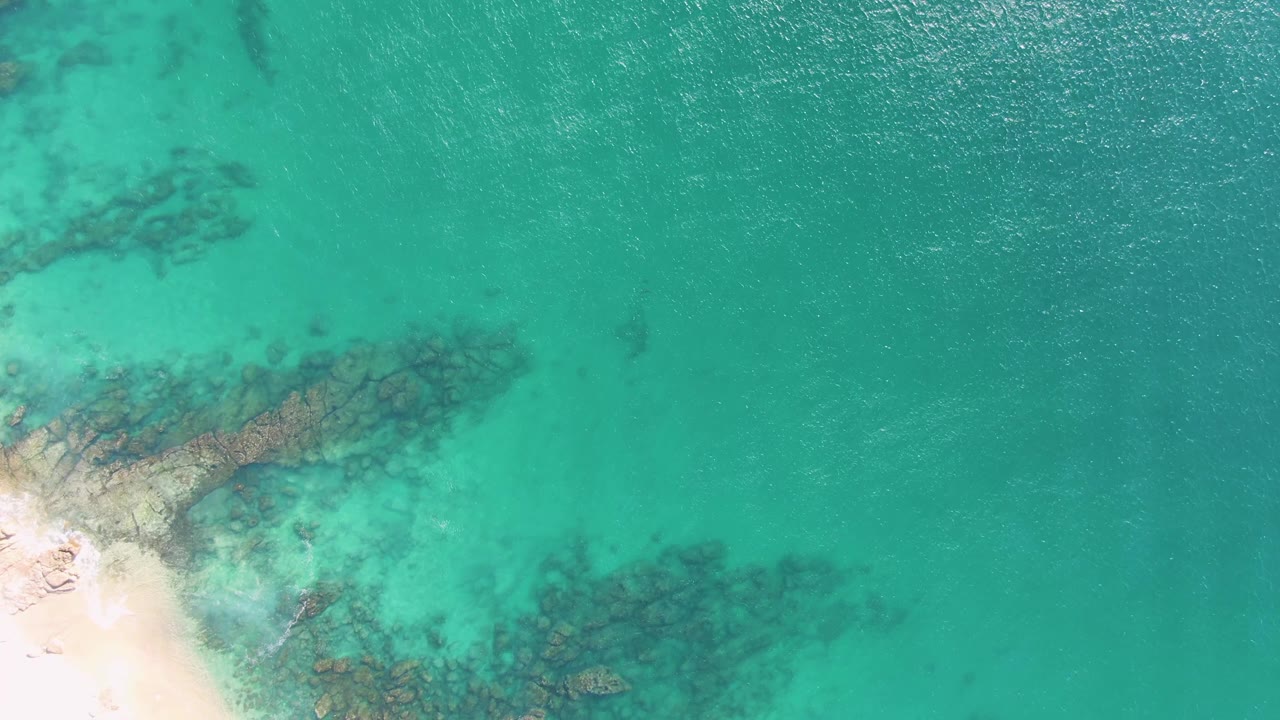 Turquoise ocean surface over submerged rocks beside a bright sandy beach edge.