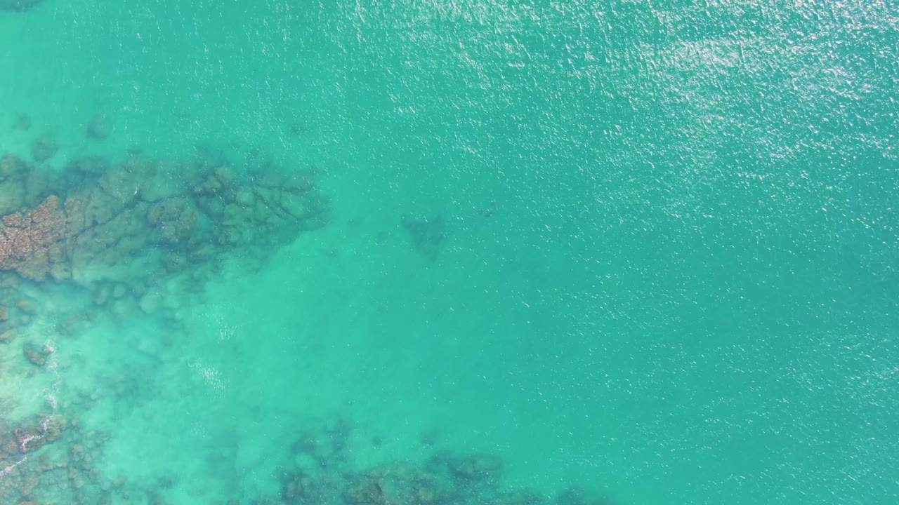 Top-down view of turquoise water at Buzzards Beach with darker underwater rocks entering from the left and no visible people.