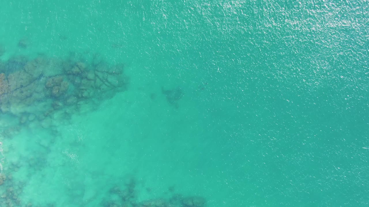 Aerial frame over Buzzards Beach water with a darker rock patch under the surface near the upper left and no visible people.