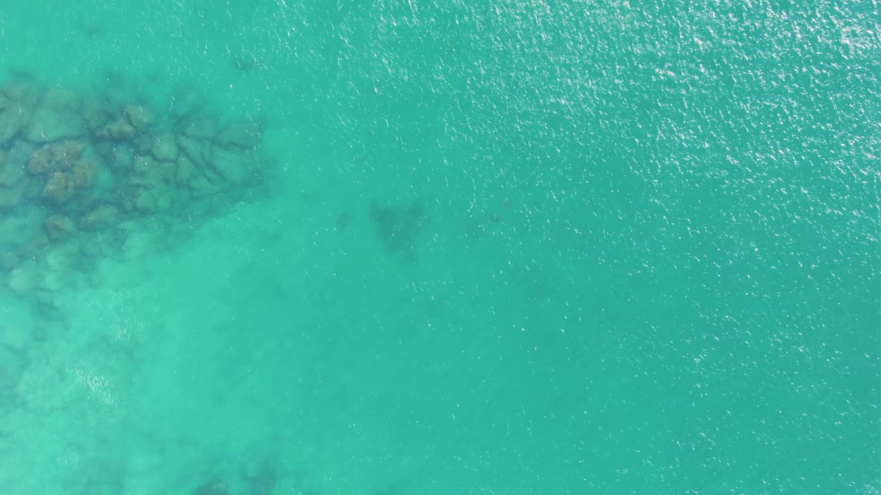 Aerial view at Buzzards Beach with submerged rocks along the left side and clear turquoise water extending across the frame, with no visible people.