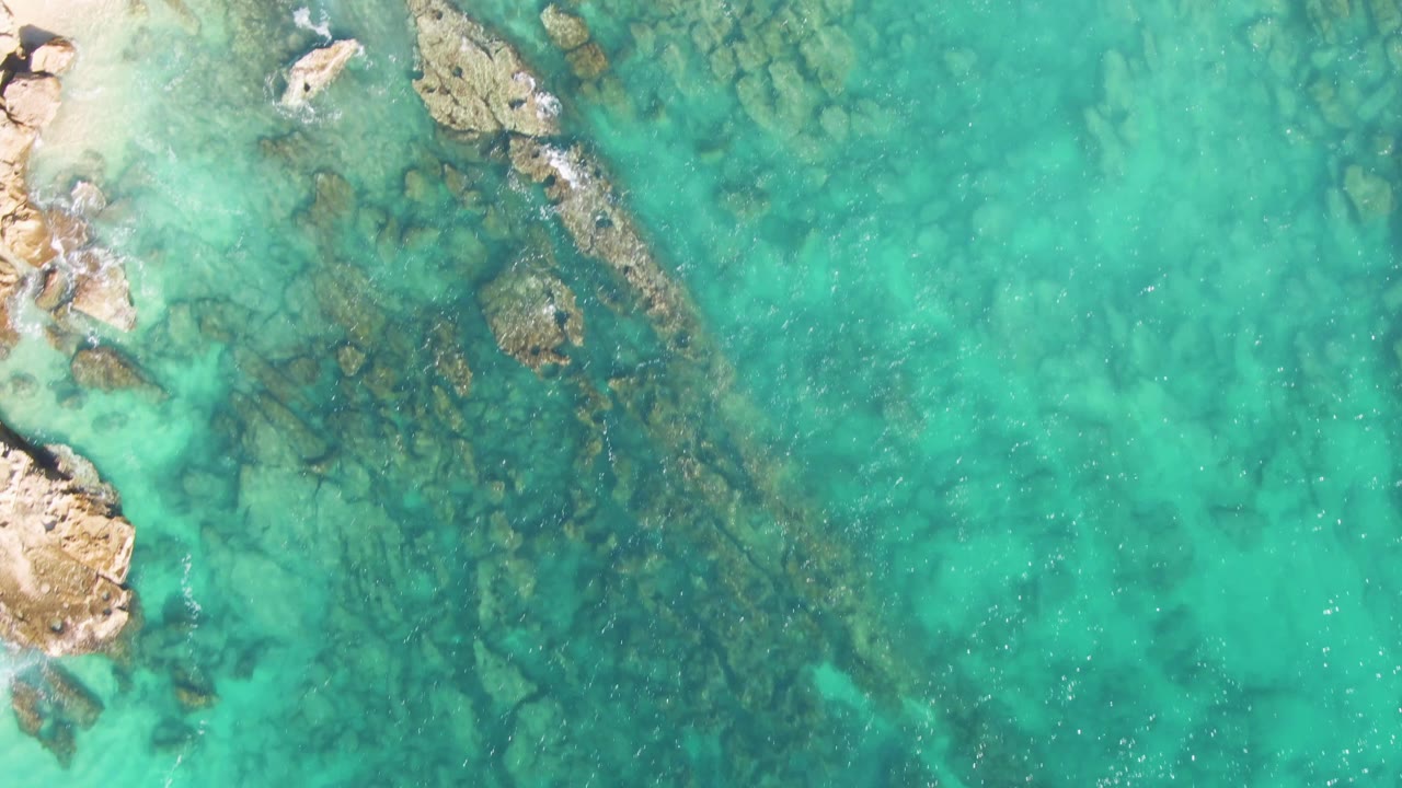 Clear turquoise water with rocky shoreline and submerged reef patches