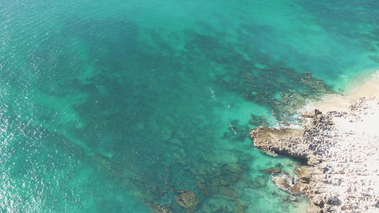 Clear teal water with underwater rocks and a rocky beach edge.