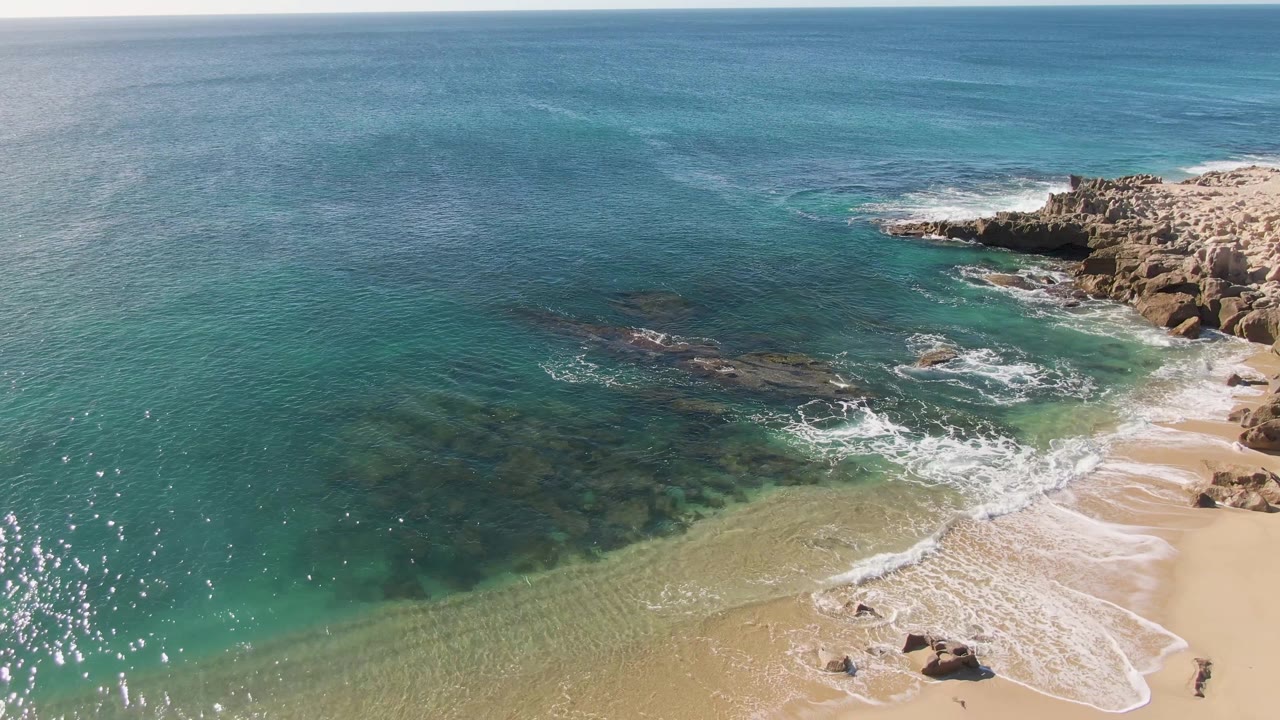 Wave foam recedes across a sandy beach beside rocky outcrops.