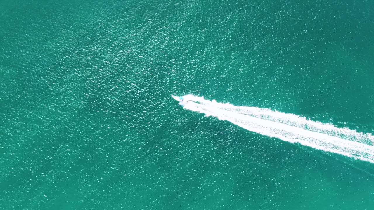 Aerial view of the speedboat moving toward the right side of the frame over rippled turquoise water at Buzzards Beach, Baja California Sur, Mexico, with no visible people.