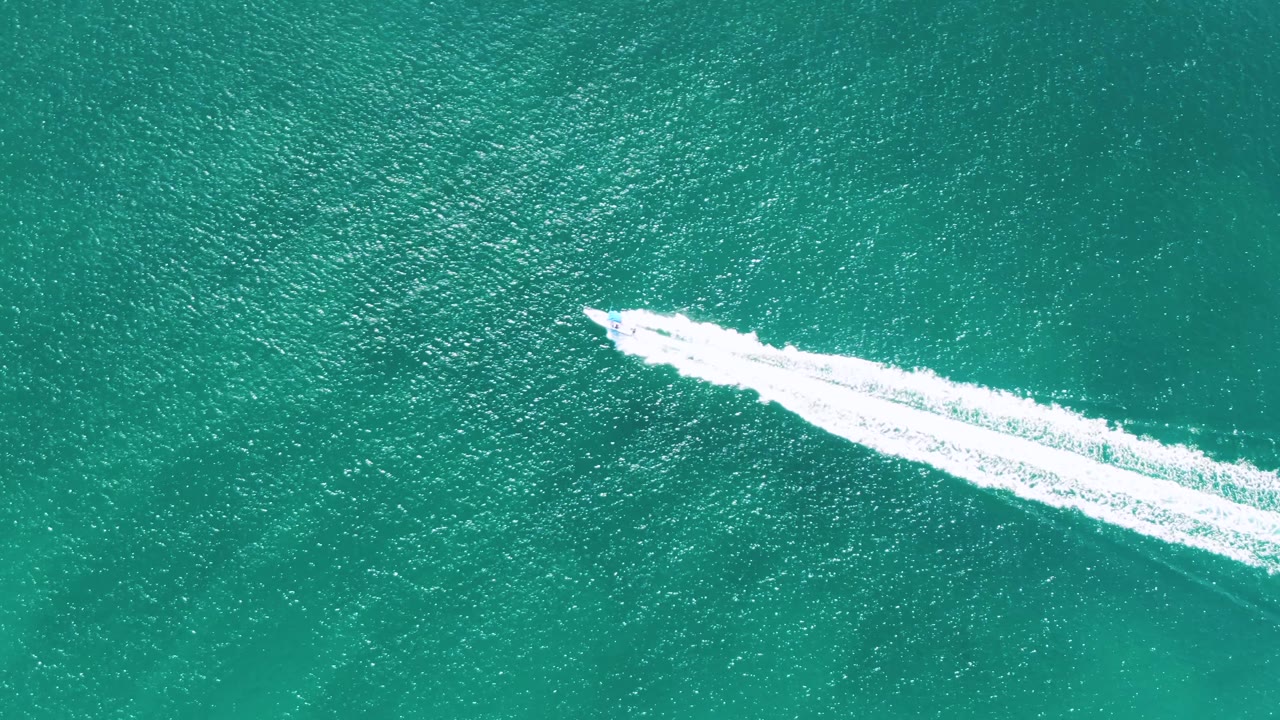 Overhead frame at Buzzards Beach, Baja California Sur, Mexico, showing the speedboat and bright diagonal wake across textured turquoise water, with no visible people.