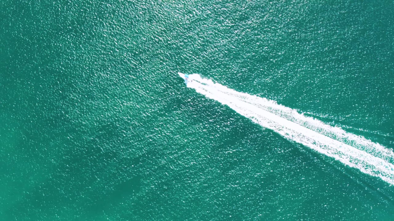 Overhead view at Buzzards Beach, Baja California Sur, Mexico, showing a speedboat entering the frame over turquoise water with a long white wake and no visible people.