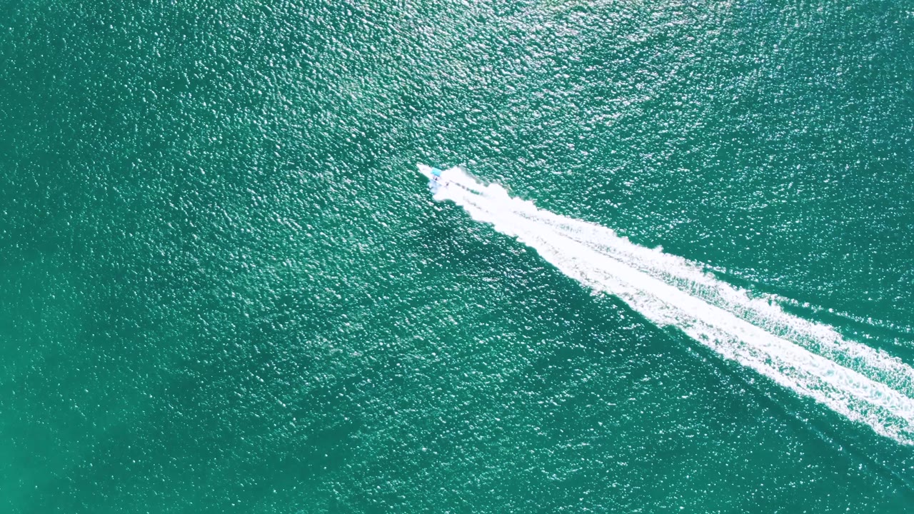 Overhead frame from Buzzards Beach, Baja California Sur, Mexico, with the speedboat farther across the turquoise sea and its white wake widening behind it, with no visible people.