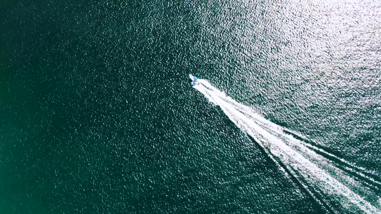 Overhead speedboat crossing blue-green ocean with white wake