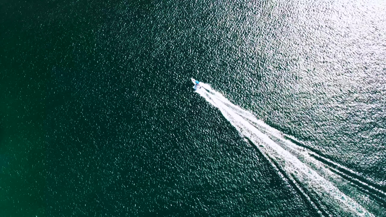 Aerial frame of the speedboat slightly farther along its diagonal path over Buzzards Beach ocean water, with parallel white wake lines and no visible people.