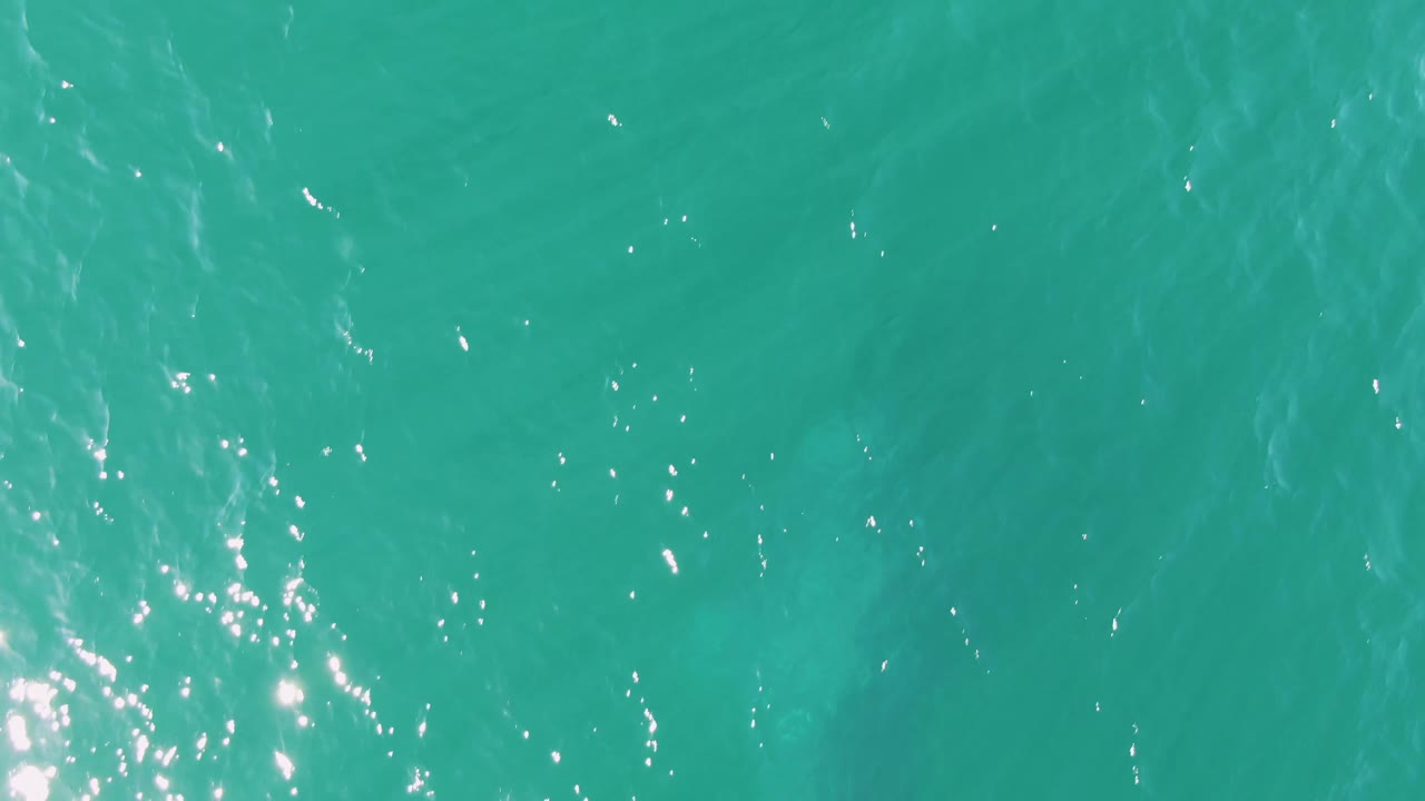 Turquoise water surface at Buzzards Beach in Baja California Sur, with a brighter cluster of sun reflections near the lower left and no visible people.