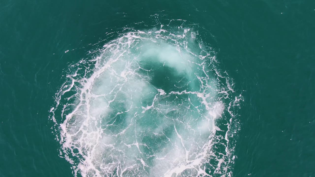 At Buzzards Beach in Baja California Sur, Mexico, the overhead view shows a larger curved foam mass forming a partial ring on teal water, with no visible people.